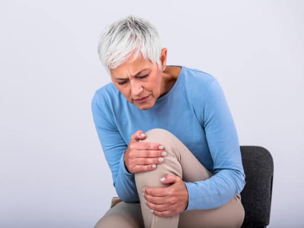 older woman grasping her knee in pain while sitting
