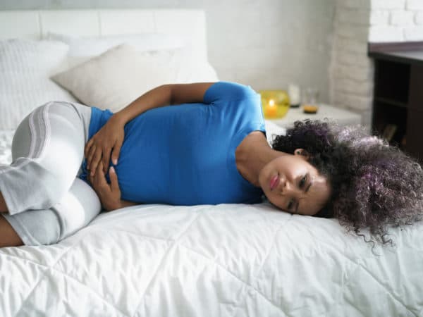 Black or Latinx woman laying on her side clearly in pain, with her hands near her groin.